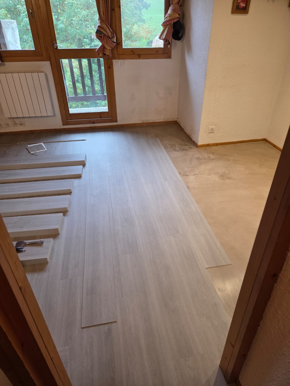 Pose de sol souple PVC en cours dans un salon avec fenêtres en bois